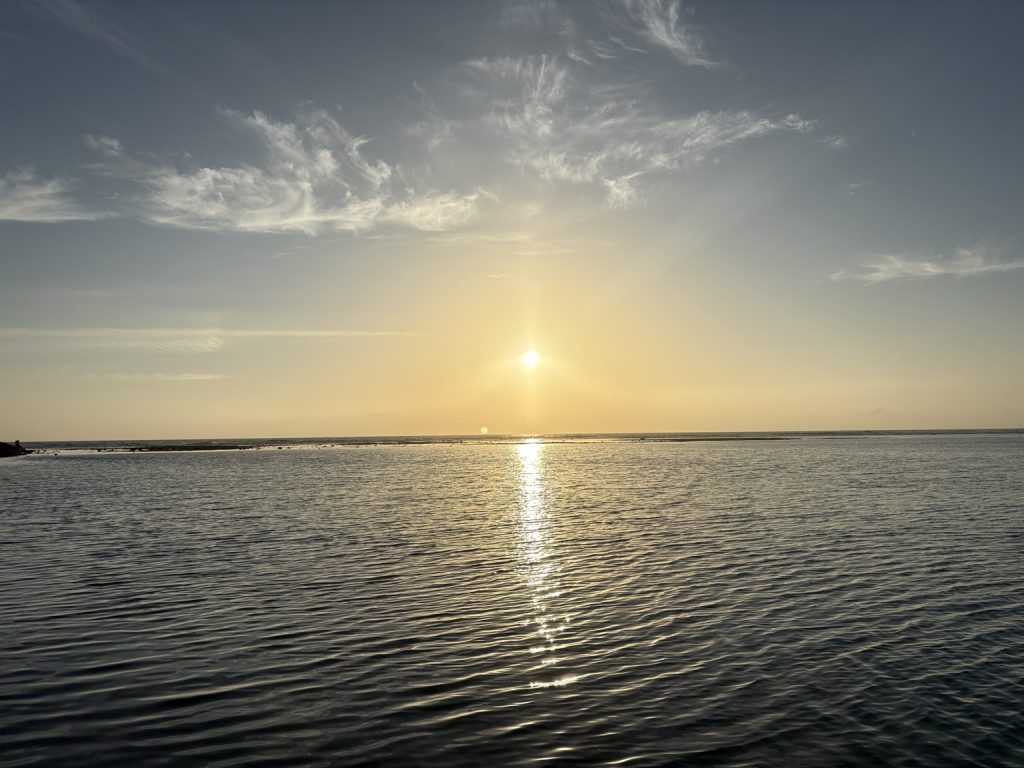 夕暮れの沖縄の海に夕日が反射し、水面に光の道が伸びている風景